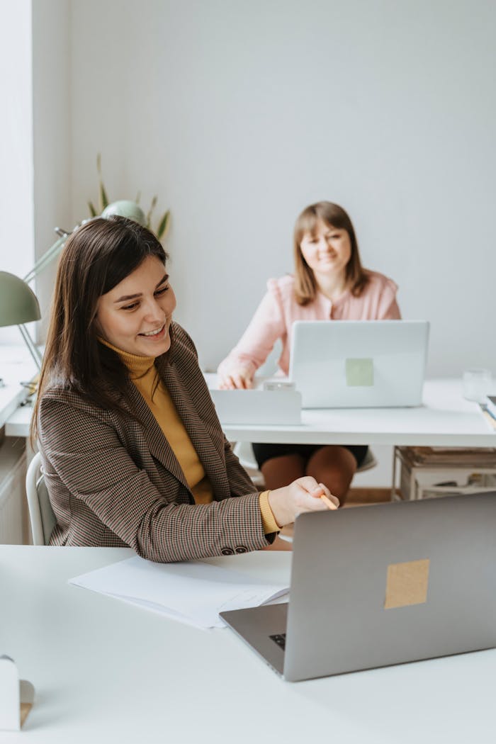 Two women working together with laptops in a bright and modern office setting.